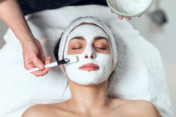 Esthetician applying a clay treatment mask during a customized facial